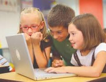 Three smiling children grouped around a laptop