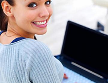  Young smiling woman looking back over her shoulder, her laptop is open in front of her.