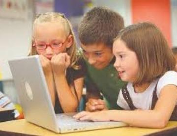 3 young learners  in a classroon, together looking at an open lptop