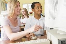A teacher or assistant is helping a smiling student as he uses his computer.