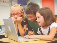 3 young learners  in a classroon, together looking at an open lptop