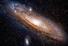 The Andromeda galaxy shown as dark space with stars and a swirling mass or ball of lights at the centre.ba
