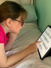 Jessica, a 10 year old girl, lying on her bed, reading on her iPad which is leaning against the wall