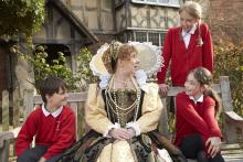 Queen Elizabeth the first outside a tudr style house with 3 modern school children