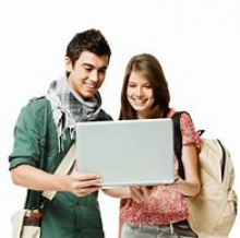 male and female young adults standing both looking at a laptop the female student is holding
