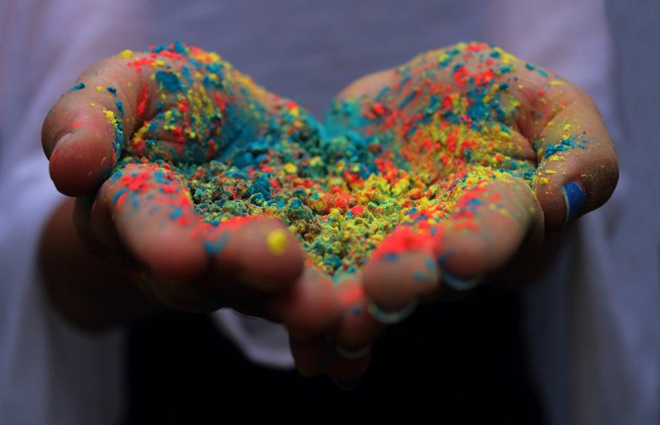 open cupped hands in shape of a heart holding powder in assorted rainbow colours