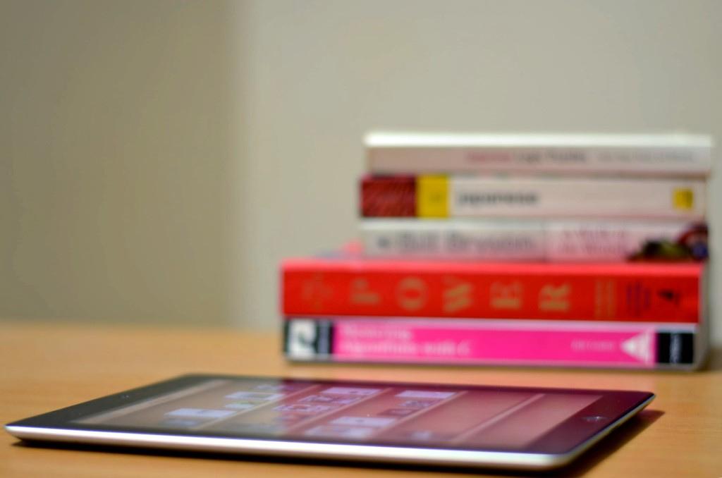 a pile of books and an iPad/tablet on a deask